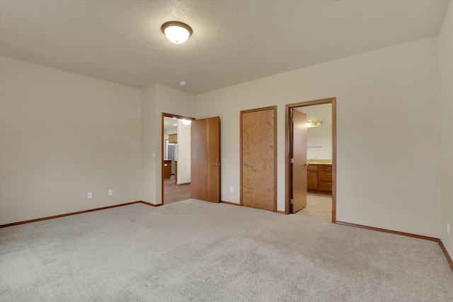 unfurnished bedroom with a textured ceiling, connected bathroom, and light colored carpet