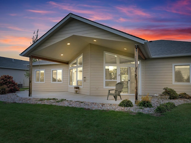 back house at dusk featuring a lawn and a patio area