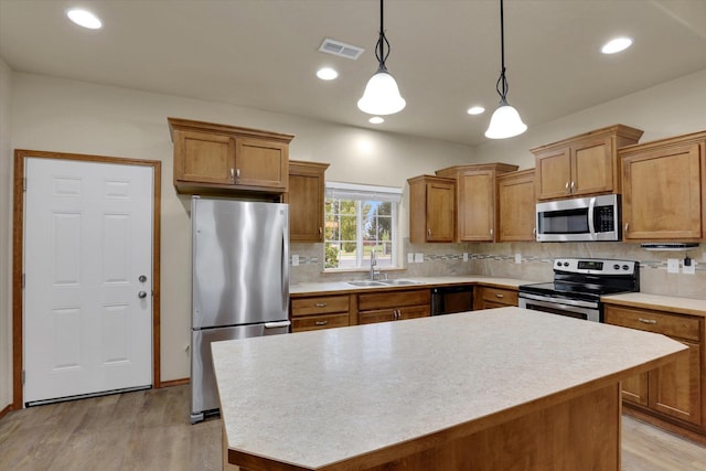 kitchen with decorative light fixtures, a kitchen island, sink, and appliances with stainless steel finishes