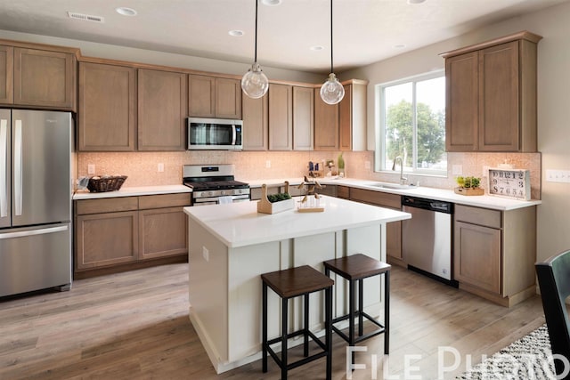 kitchen featuring sink, hanging light fixtures, light hardwood / wood-style floors, a kitchen island, and appliances with stainless steel finishes