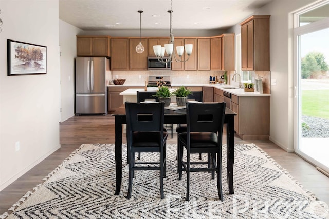 kitchen with light wood-type flooring, backsplash, stainless steel appliances, sink, and pendant lighting