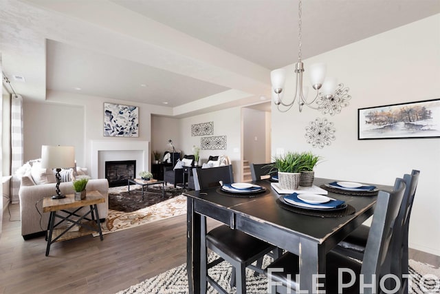 dining area with hardwood / wood-style flooring, a raised ceiling, and a chandelier