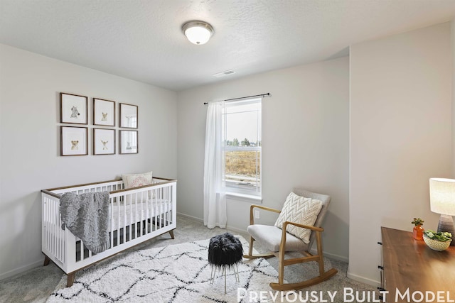 carpeted bedroom with a textured ceiling and a nursery area