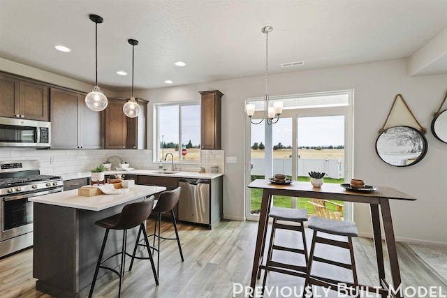 kitchen with dark brown cabinetry, a center island, an inviting chandelier, decorative light fixtures, and appliances with stainless steel finishes