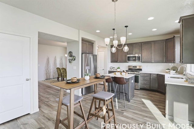 kitchen featuring sink, stainless steel appliances, tasteful backsplash, pendant lighting, and light wood-type flooring