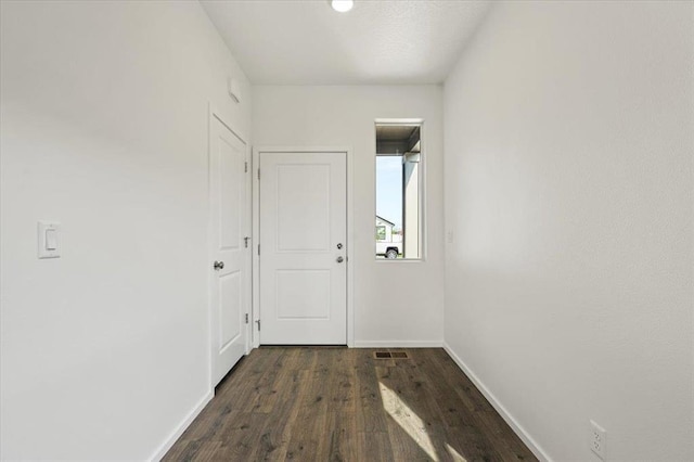 doorway with dark wood-style floors, visible vents, and baseboards