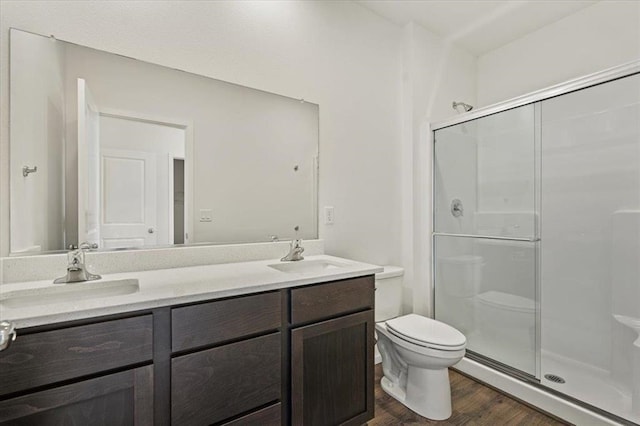 bathroom featuring a stall shower, a sink, toilet, and wood finished floors