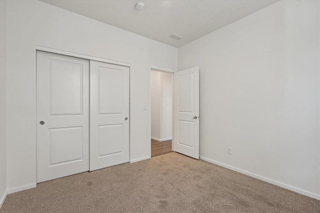 unfurnished bedroom with a closet, light colored carpet, visible vents, and baseboards