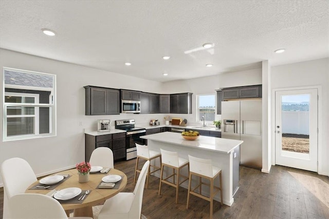 kitchen featuring stainless steel appliances, dark wood-style flooring, a sink, and a center island