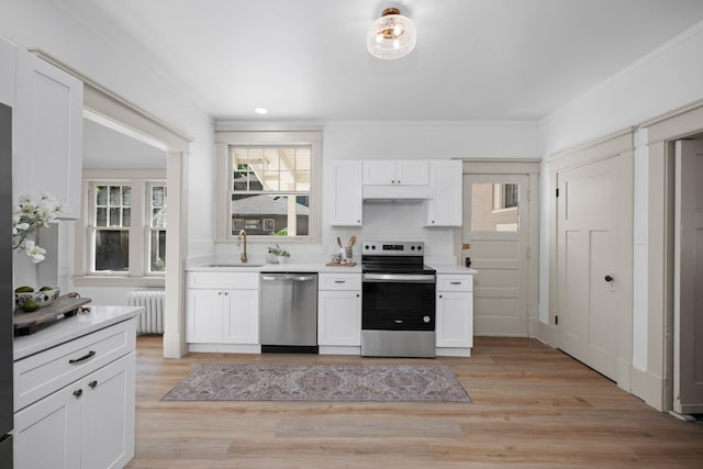 kitchen with light wood-type flooring, radiator, stainless steel appliances, sink, and white cabinetry