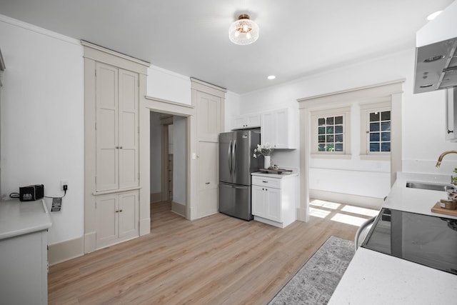 kitchen with stove, white cabinetry, sink, and stainless steel refrigerator