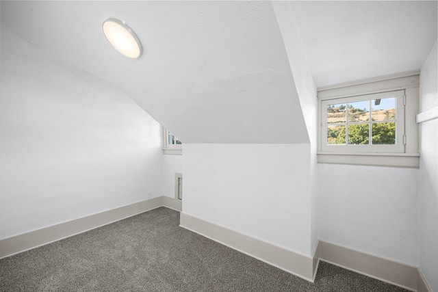 additional living space featuring dark carpet and vaulted ceiling