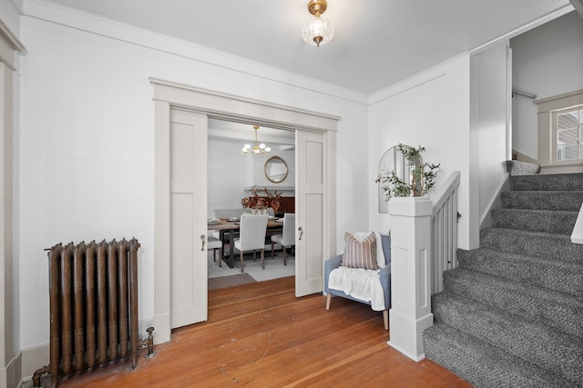 interior space with radiator, wood-type flooring, a notable chandelier, and ornamental molding