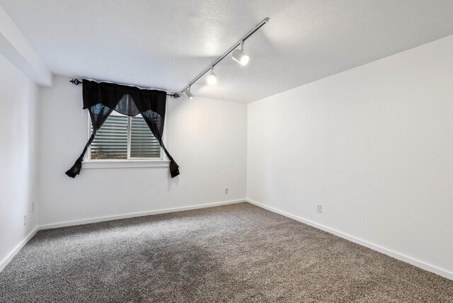 carpeted empty room featuring a textured ceiling and track lighting