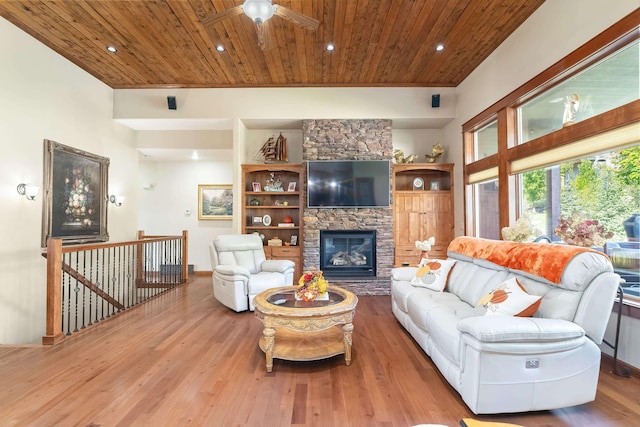 living room featuring wood-type flooring, a stone fireplace, ceiling fan, and wooden ceiling