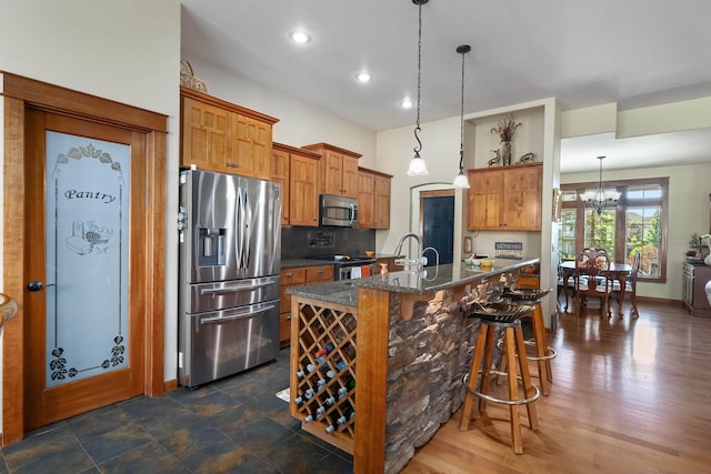 kitchen featuring stainless steel appliances, a kitchen breakfast bar, a notable chandelier, pendant lighting, and a center island with sink