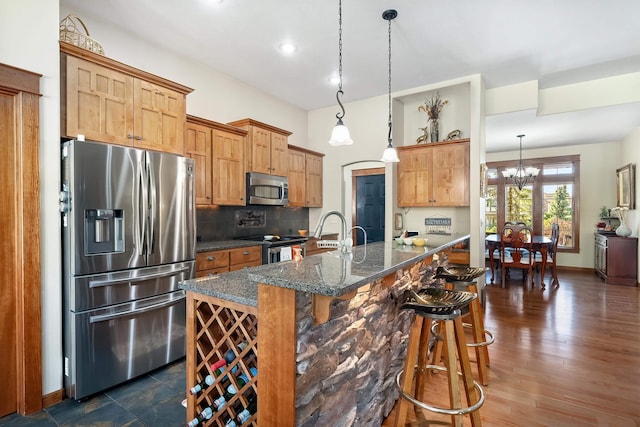 kitchen featuring a kitchen bar, stainless steel appliances, hanging light fixtures, and dark stone countertops