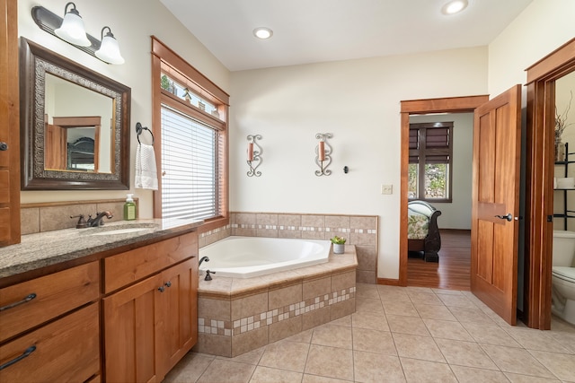 bathroom with tile patterned floors, vanity, a relaxing tiled tub, and toilet