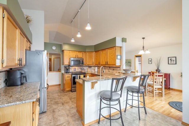 kitchen featuring kitchen peninsula, light stone countertops, backsplash, stainless steel appliances, and pendant lighting