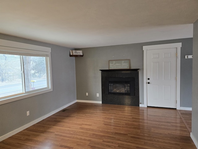 unfurnished living room with baseboards, wood finished floors, and a glass covered fireplace