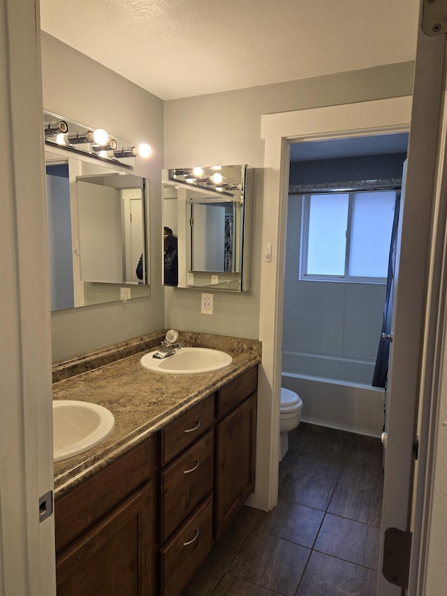 full bath with a sink, toilet, double vanity, and a textured ceiling