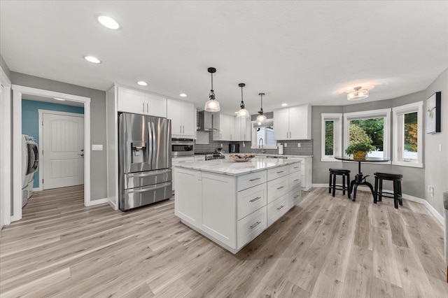 kitchen with a center island, wall chimney range hood, light stone counters, white cabinetry, and stainless steel appliances