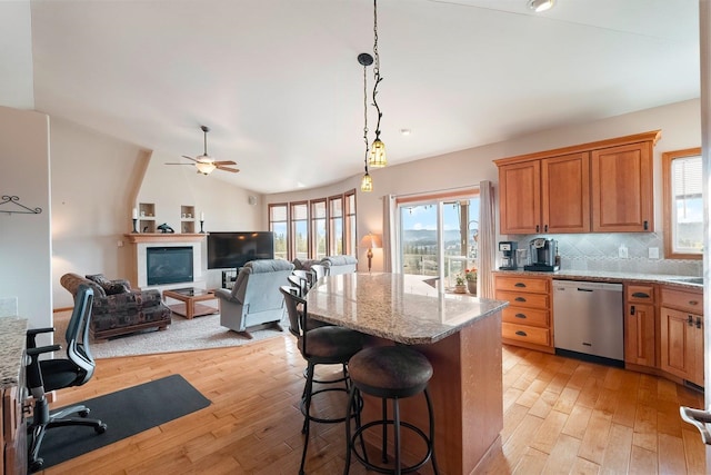 kitchen featuring light stone countertops, dishwasher, vaulted ceiling, a breakfast bar, and light wood-type flooring