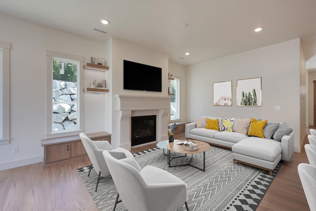 living area featuring visible vents, light wood finished floors, baseboards, recessed lighting, and a glass covered fireplace