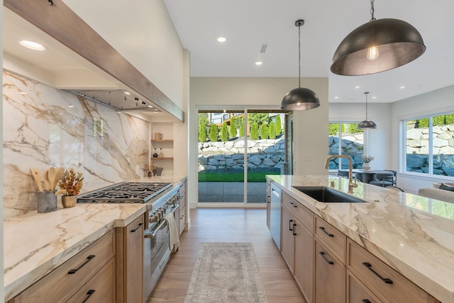 kitchen featuring light stone counters, appliances with stainless steel finishes, wall chimney exhaust hood, and a sink