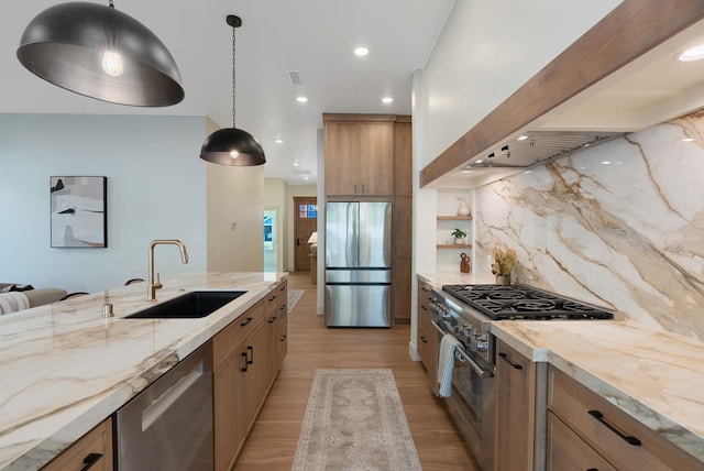 kitchen featuring tasteful backsplash, appliances with stainless steel finishes, light wood-style floors, wall chimney exhaust hood, and a sink