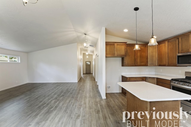 kitchen with hardwood / wood-style floors, hanging light fixtures, vaulted ceiling, appliances with stainless steel finishes, and a kitchen island