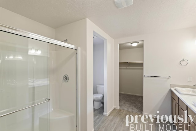 bathroom with hardwood / wood-style floors, a textured ceiling, toilet, and a shower with door