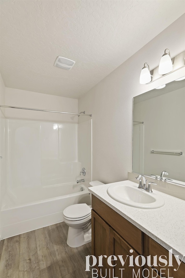 full bathroom featuring hardwood / wood-style floors, a textured ceiling,  shower combination, toilet, and vanity