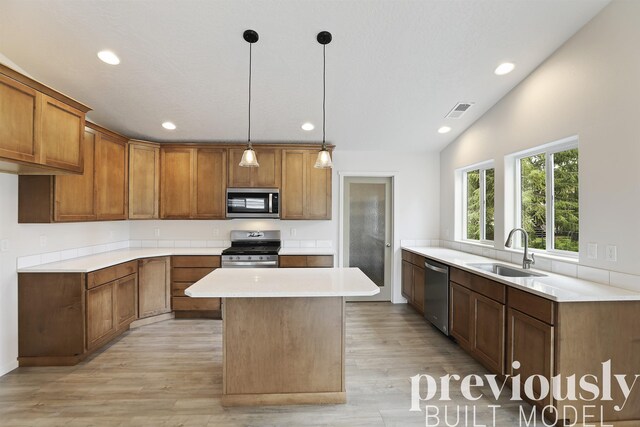 kitchen with appliances with stainless steel finishes, sink, pendant lighting, light hardwood / wood-style flooring, and a center island