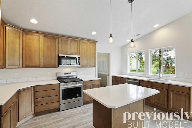 kitchen with sink, hanging light fixtures, stainless steel appliances, light hardwood / wood-style floors, and a kitchen island