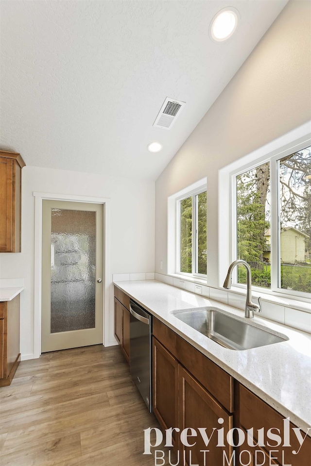 kitchen featuring light stone countertops, sink, stainless steel dishwasher, vaulted ceiling, and light wood-type flooring