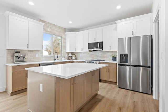 kitchen featuring tasteful backsplash, stainless steel appliances, light hardwood / wood-style flooring, a center island, and white cabinetry