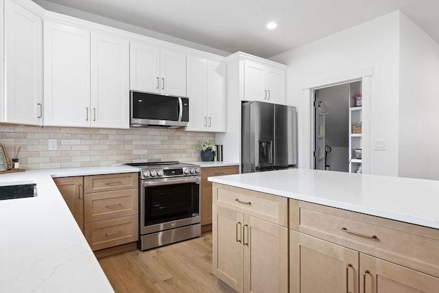 kitchen featuring appliances with stainless steel finishes, light wood-type flooring, backsplash, light brown cabinetry, and white cabinetry