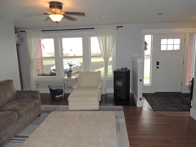 living room with ceiling fan, a wood stove, and dark wood-type flooring