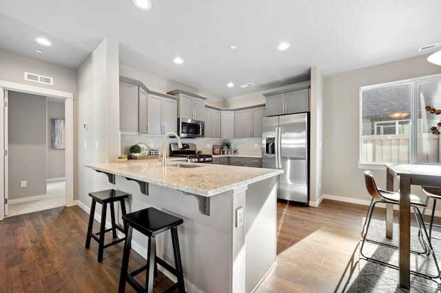 kitchen featuring light stone countertops, appliances with stainless steel finishes, dark wood-type flooring, and a breakfast bar area