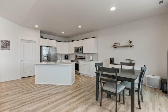 kitchen with white cabinetry, backsplash, an island with sink, light hardwood / wood-style floors, and appliances with stainless steel finishes