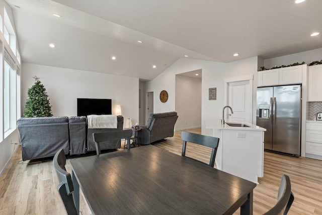 dining space with light hardwood / wood-style floors, sink, and vaulted ceiling