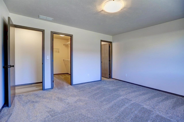 unfurnished bedroom featuring a spacious closet, a closet, light colored carpet, and a textured ceiling