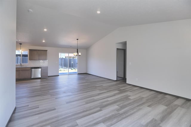 unfurnished living room featuring sink, a chandelier, lofted ceiling, and light wood-type flooring