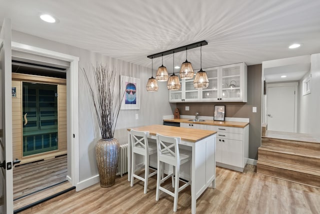 bar featuring white cabinetry, sink, light hardwood / wood-style flooring, butcher block countertops, and decorative light fixtures