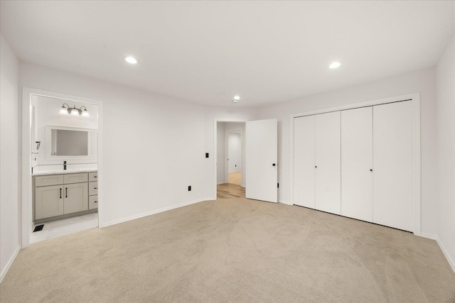 unfurnished bedroom with ensuite bathroom, a closet, light colored carpet, and sink