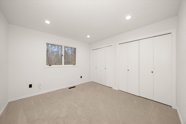 unfurnished bedroom with light carpet and two closets