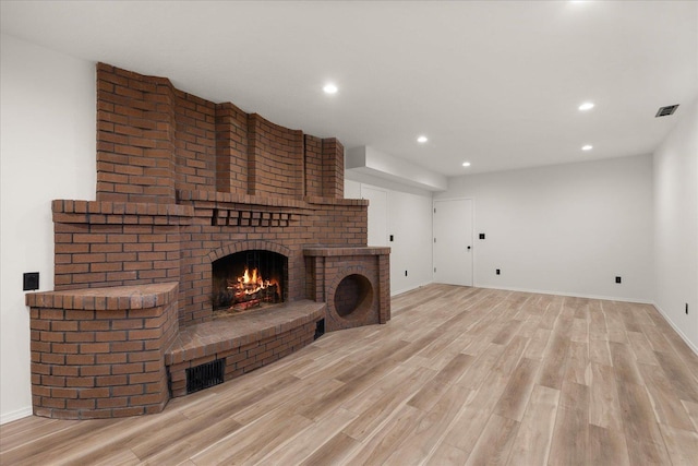 unfurnished living room with light wood-type flooring and a brick fireplace