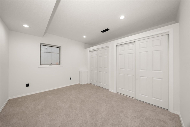 unfurnished bedroom featuring a textured ceiling, light carpet, and multiple closets