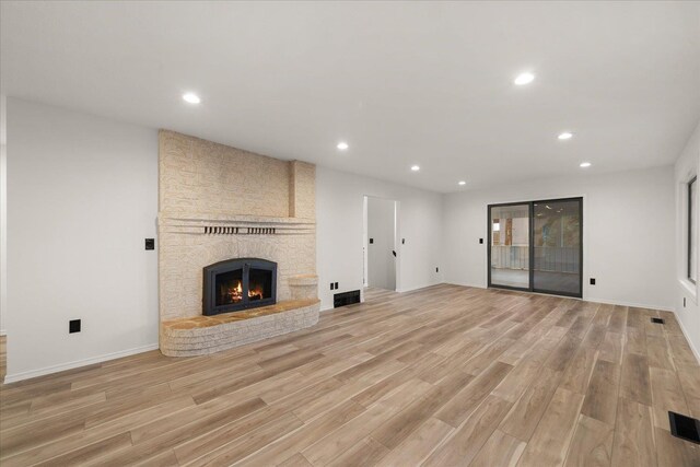 unfurnished living room with light wood-type flooring and a brick fireplace